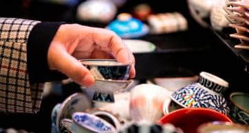 Store display closeup of ceramic pottery with tea cups teacups design and hand person picking buying in Kyoto, Japan Nishiki market street